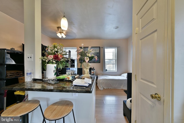 kitchen featuring light hardwood / wood-style floors, a kitchen bar, kitchen peninsula, dark stone countertops, and hanging light fixtures