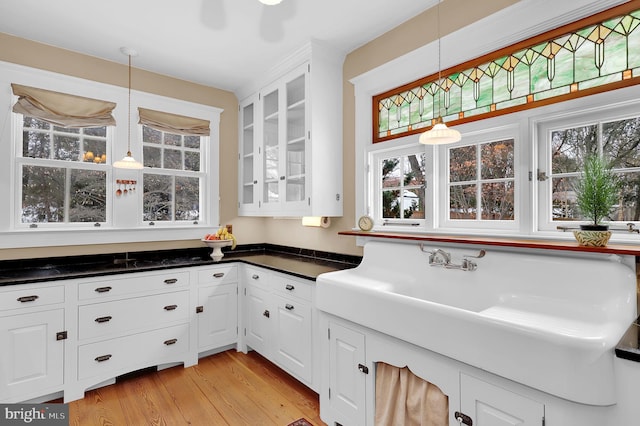 kitchen with hanging light fixtures, light wood-type flooring, dark countertops, and white cabinetry