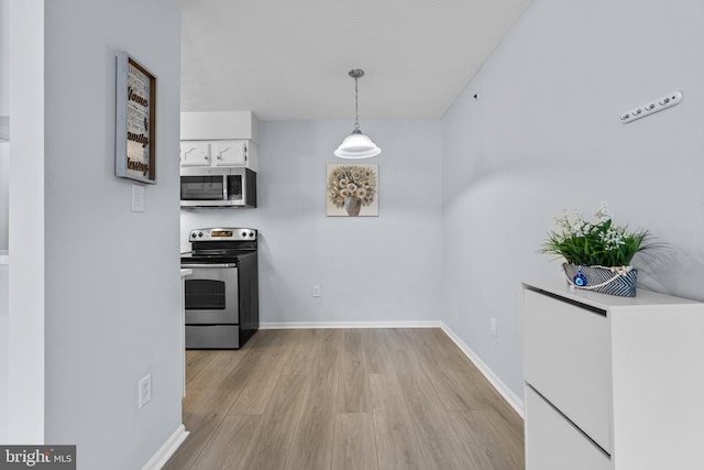 kitchen featuring hanging light fixtures, white cabinetry, appliances with stainless steel finishes, and light wood-type flooring