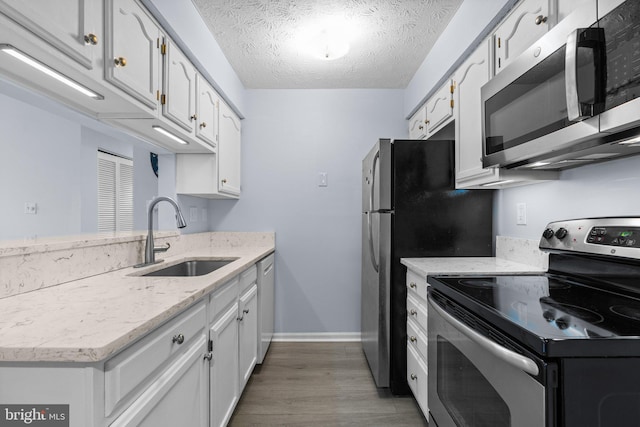 kitchen with sink, stainless steel appliances, wood-type flooring, a textured ceiling, and white cabinets