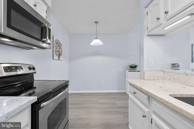 kitchen with appliances with stainless steel finishes, white cabinetry, hanging light fixtures, light stone counters, and light wood-type flooring