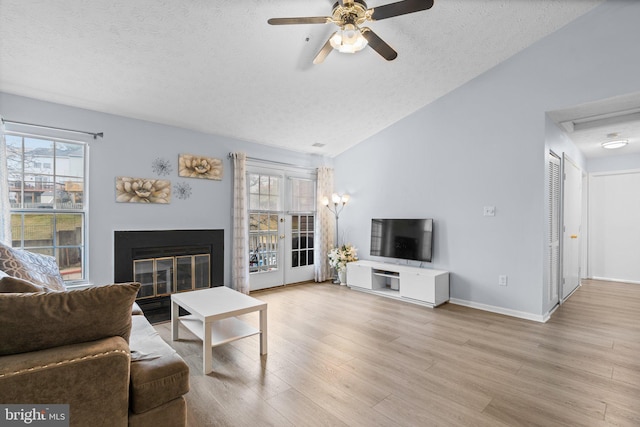 living room with lofted ceiling, ceiling fan, a textured ceiling, and light wood-type flooring