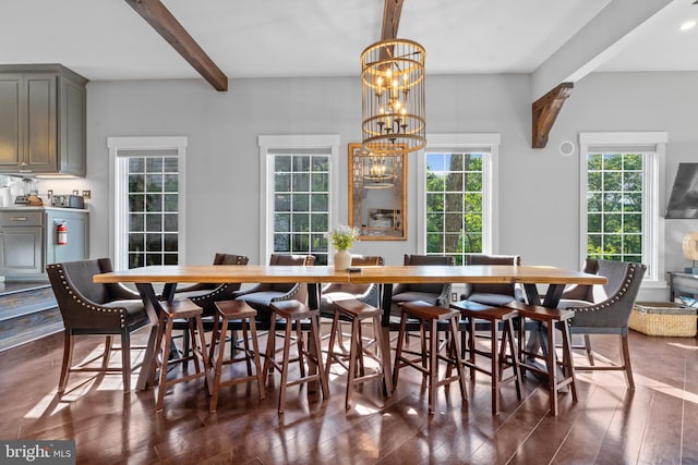 dining room featuring dark wood-type flooring, a healthy amount of sunlight, a notable chandelier, and beamed ceiling