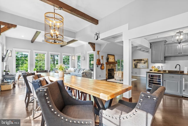 dining area featuring dark wood-type flooring, a stone fireplace, an inviting chandelier, wine cooler, and sink