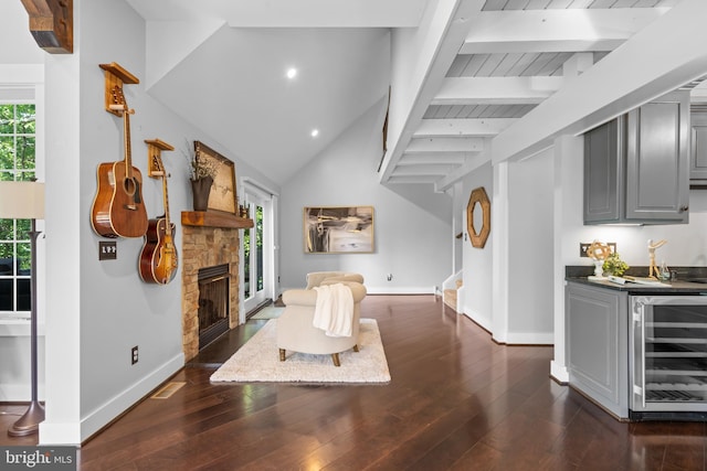 living room with bar, a stone fireplace, dark wood-type flooring, beverage cooler, and beamed ceiling