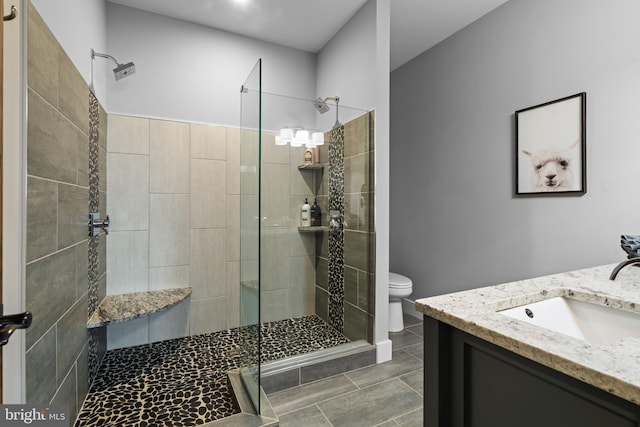 bathroom with toilet, a tile shower, tile patterned floors, and vanity