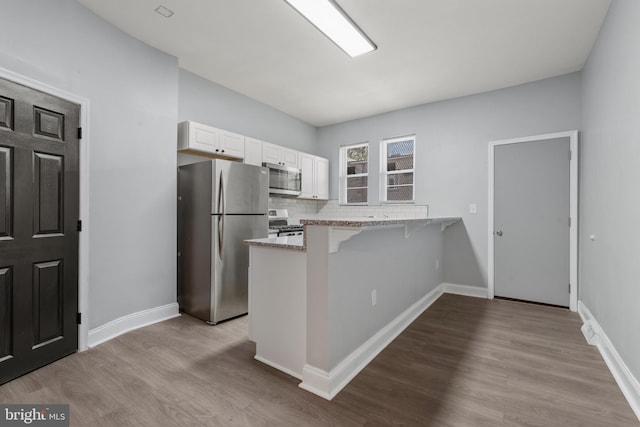 kitchen with white cabinets, stainless steel appliances, light hardwood / wood-style floors, a kitchen breakfast bar, and kitchen peninsula