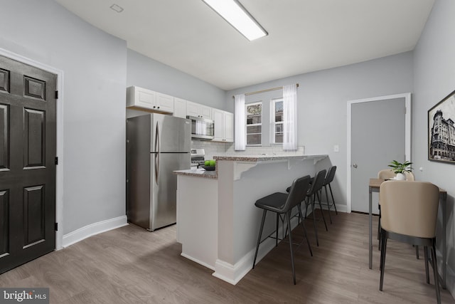 kitchen with white cabinetry, light hardwood / wood-style floors, kitchen peninsula, a breakfast bar area, and appliances with stainless steel finishes