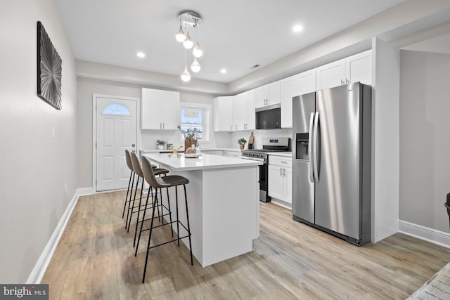 kitchen featuring an island with sink, white cabinets, decorative backsplash, hanging light fixtures, and stainless steel appliances