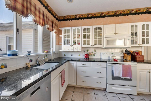 kitchen featuring light tile patterned flooring, sink, dark stone countertops, white cabinets, and white appliances