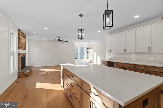 kitchen featuring decorative light fixtures, decorative backsplash, light wood-style floors, open floor plan, and a stone fireplace