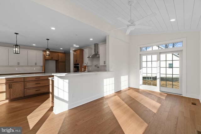 kitchen featuring backsplash, light countertops, wall chimney range hood, and wood finished floors