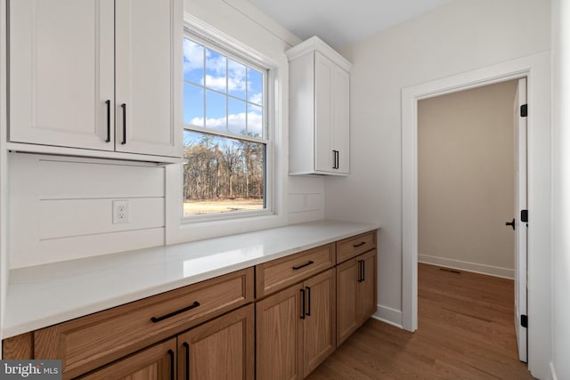 kitchen featuring light wood-type flooring, light countertops, baseboards, and white cabinetry