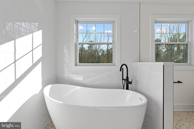 bathroom featuring a soaking tub, a wealth of natural light, and tile walls