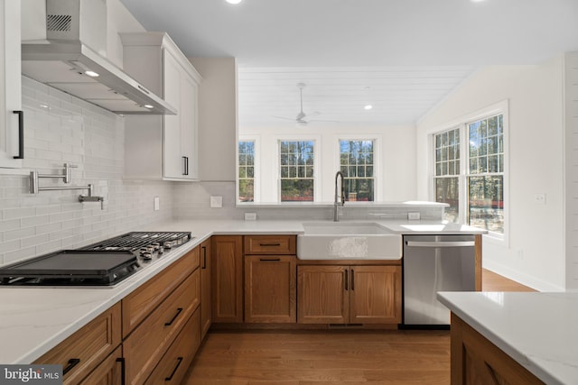 kitchen with stainless steel appliances, a sink, wall chimney exhaust hood, tasteful backsplash, and brown cabinetry