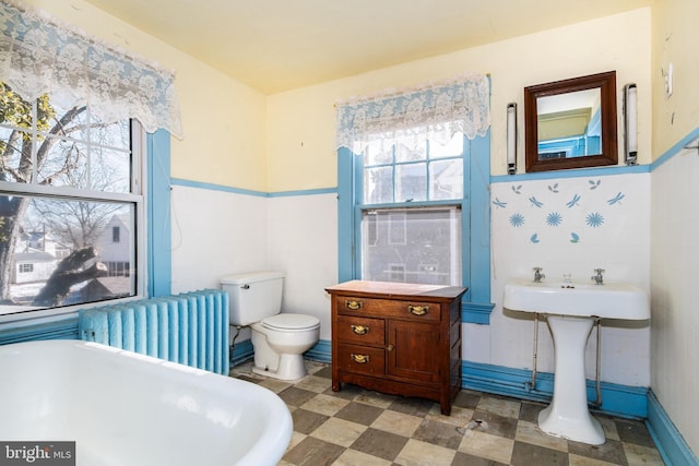 bathroom with radiator heating unit, a tub, and toilet