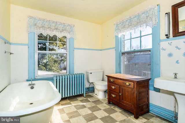 bathroom with a washtub, radiator, a wealth of natural light, and toilet