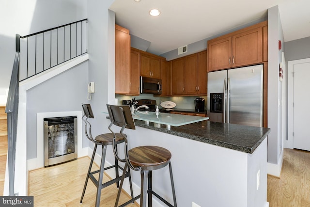 kitchen featuring a breakfast bar, dark stone countertops, light hardwood / wood-style floors, kitchen peninsula, and stainless steel appliances