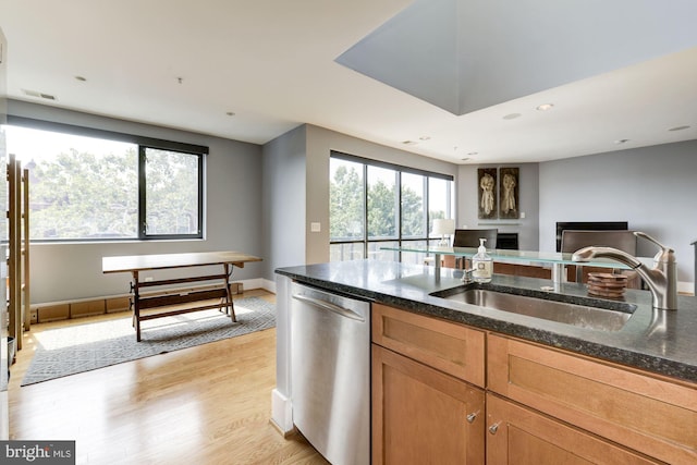 kitchen with dishwasher, sink, light wood-type flooring, and dark stone counters