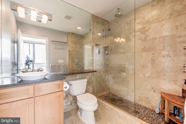 bathroom with vanity, a tile shower, tile walls, and toilet