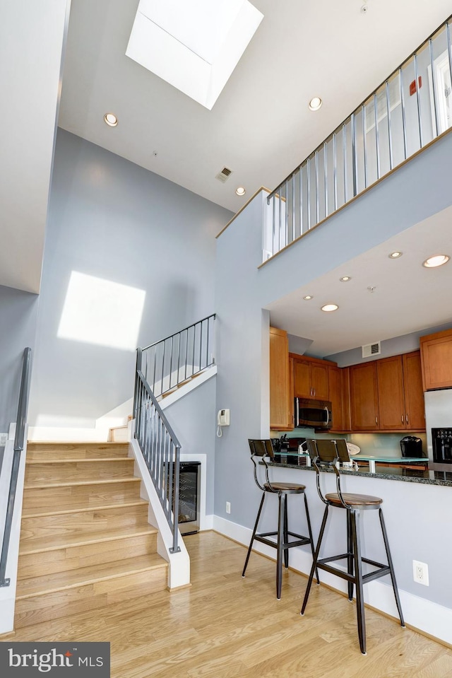 kitchen with a towering ceiling, a kitchen bar, a skylight, and light hardwood / wood-style floors