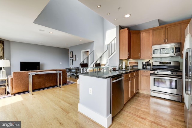 kitchen with appliances with stainless steel finishes, sink, dark stone counters, kitchen peninsula, and light hardwood / wood-style flooring