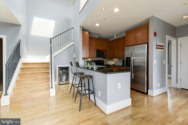 kitchen with a breakfast bar, light wood-type flooring, appliances with stainless steel finishes, kitchen peninsula, and dark stone counters