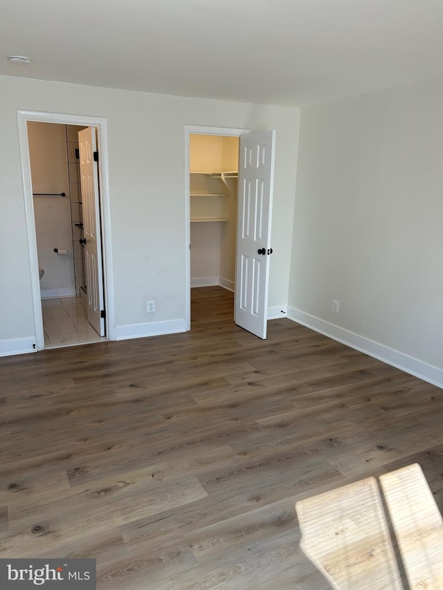 unfurnished bedroom featuring ensuite bathroom, a walk in closet, a closet, and hardwood / wood-style floors