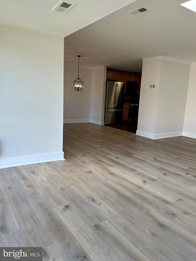 unfurnished living room featuring crown molding, an inviting chandelier, and light hardwood / wood-style floors