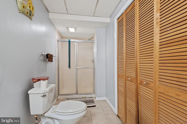 bathroom with tile patterned floors, a drop ceiling, toilet, and an enclosed shower