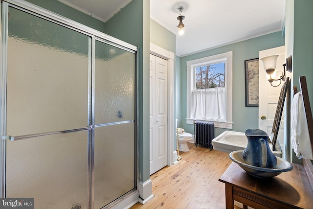 bathroom with crown molding, hardwood / wood-style flooring, radiator heating unit, a shower with shower door, and toilet