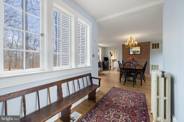 hall with beamed ceiling, radiator heating unit, a chandelier, and light hardwood / wood-style floors