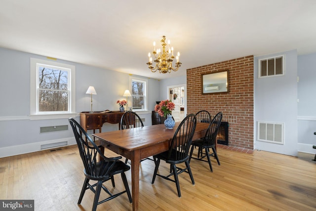 dining room with a brick fireplace, a chandelier, and light wood-type flooring