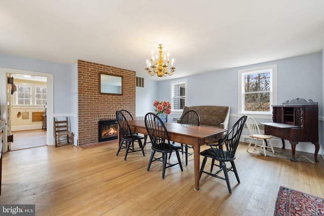 dining area with a notable chandelier, plenty of natural light, a brick fireplace, and light wood-type flooring