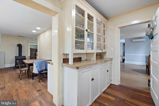 kitchen with crown molding, dark wood-type flooring, a wall mounted AC, and white cabinets