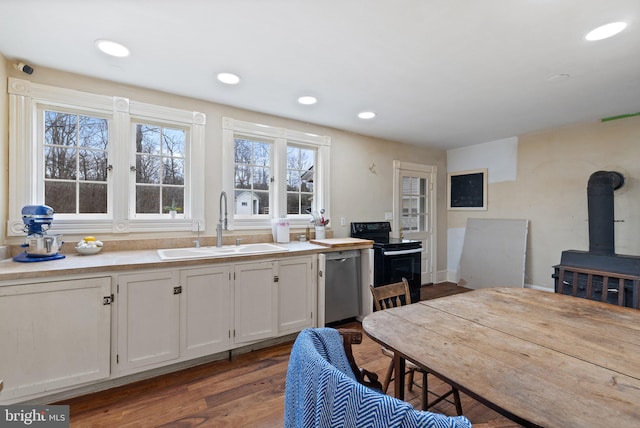 kitchen featuring sink, white cabinetry, a wood stove, electric range, and stainless steel dishwasher