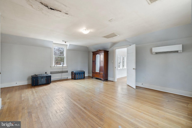 unfurnished living room featuring lofted ceiling, a wall unit AC, and light wood-type flooring