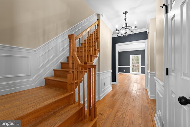 staircase with hardwood / wood-style flooring, crown molding, and a notable chandelier