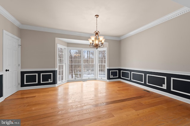 unfurnished dining area featuring light hardwood / wood-style flooring, crown molding, and a chandelier