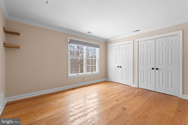 unfurnished bedroom with crown molding, multiple closets, and light wood-type flooring