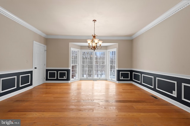 unfurnished dining area featuring hardwood / wood-style floors, ornamental molding, and an inviting chandelier