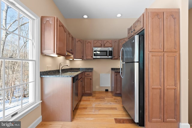 kitchen featuring sink, light hardwood / wood-style flooring, dark stone counters, and stainless steel appliances