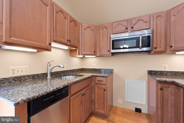 kitchen featuring sink, light wood-type flooring, dark stone countertops, and appliances with stainless steel finishes