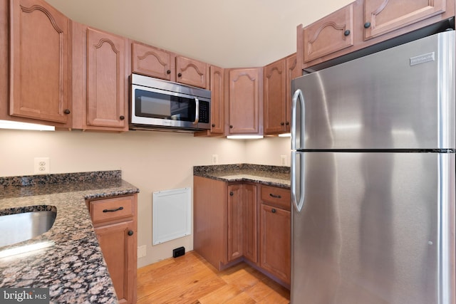 kitchen with light hardwood / wood-style floors, sink, stainless steel appliances, and dark stone countertops