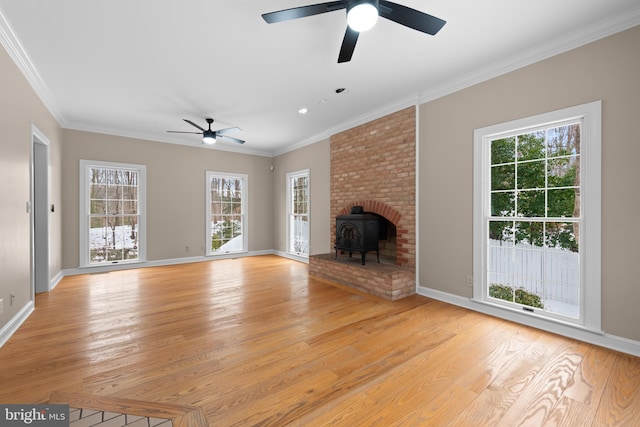 unfurnished living room with light wood-type flooring, a wood stove, ceiling fan, and ornamental molding