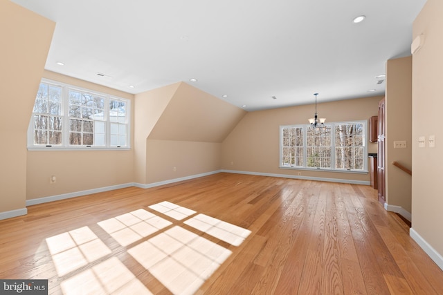 additional living space with a chandelier, a healthy amount of sunlight, light hardwood / wood-style floors, and lofted ceiling