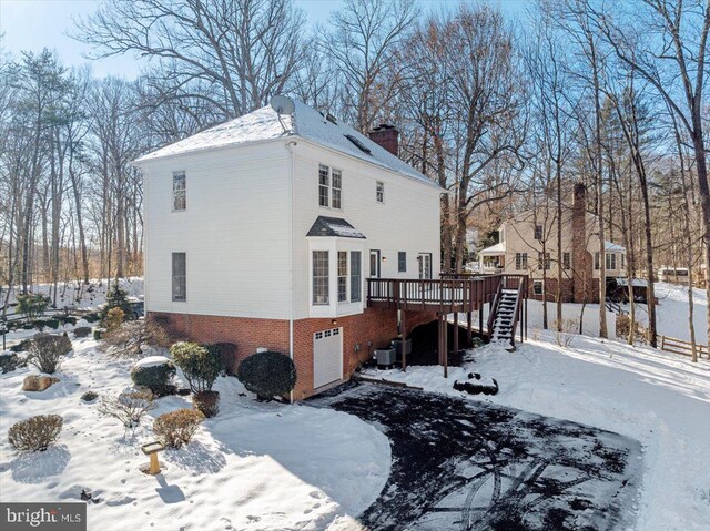 snow covered property with a garage, a wooden deck, and central AC