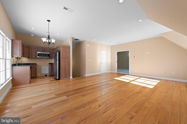 unfurnished living room featuring light hardwood / wood-style floors, plenty of natural light, sink, and a chandelier