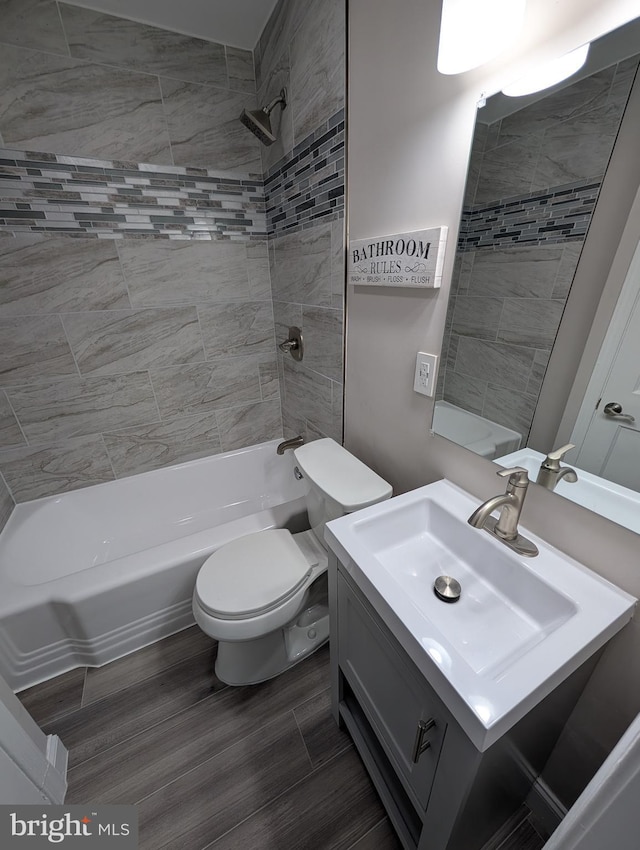 full bathroom featuring hardwood / wood-style flooring, tiled shower / bath combo, vanity, and toilet