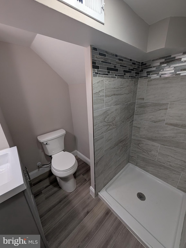 bathroom with toilet, a tile shower, wood-type flooring, and vanity